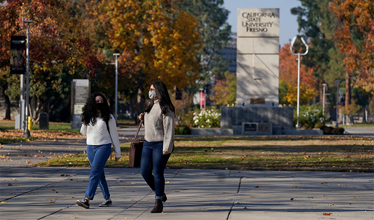 Two young women in masks walk across campus.