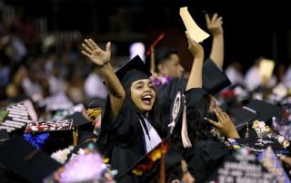 Hispanic student raises her arms triumphantly at commencement ceremony