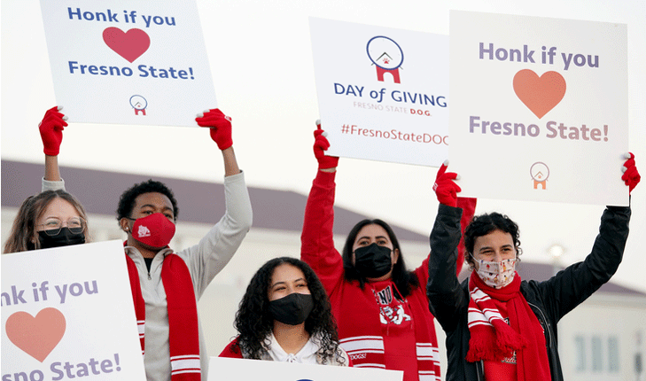Students hold signs up in front of Save Mart Center for Day of Giving.