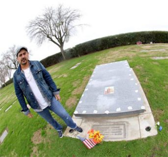 Author Tim Z. Hernandez with the monument installed in 2013 at Holy Cross Cemetery bearing the names of the 28 migrants killed.