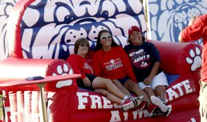 Fresno State alumni on large, inflatable Bulldogs chair at tailgate party.