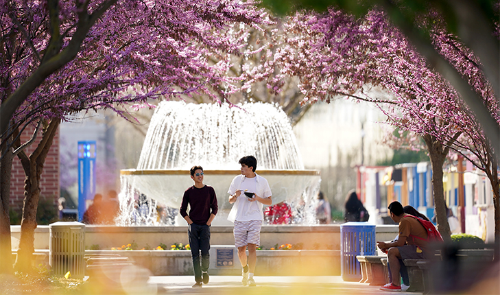 Two students walk in front of the fountain at Fresno State.