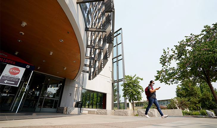 Student walking in front of the Henry Madden Library.