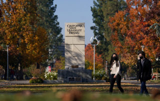 Masked students walk in front the Fresno State sign.