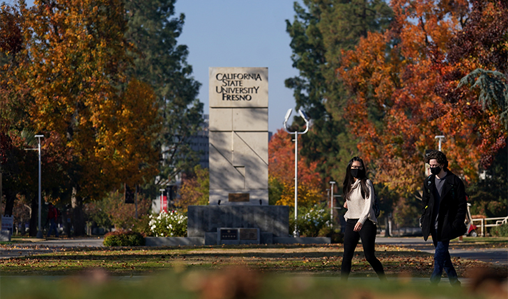 Masked students walk in front the Fresno State sign.