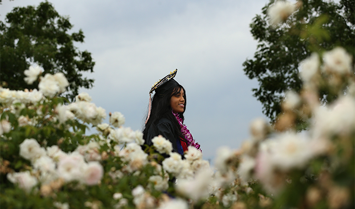 Fresno State graduate stands in front of flowers.