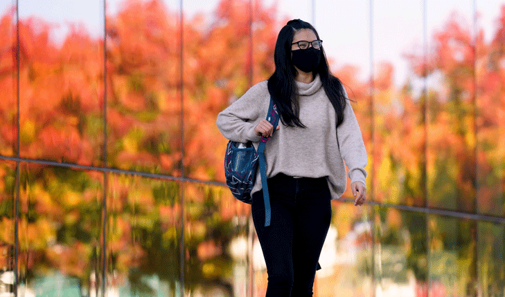 Student walks on campus wearing face mask during COVID-19 pandemic.
