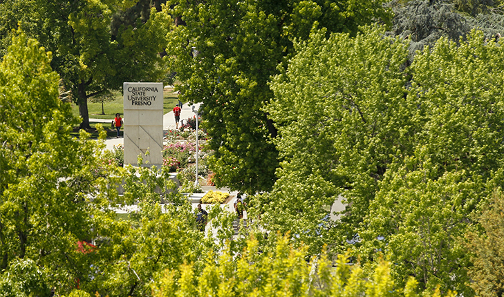 California State University, Fresno monument on campus seen through the green trees.