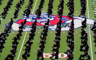 Graduates sit on Bulldog Stadium turf, distanced apart from one another.