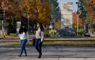 Two young women in masks walk across campus.