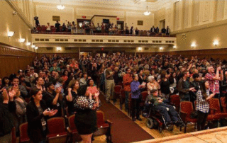 A crowd gathers inside an auditorium for an artistic performance