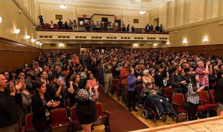 A crowd gathers inside an auditorium for an artistic performance