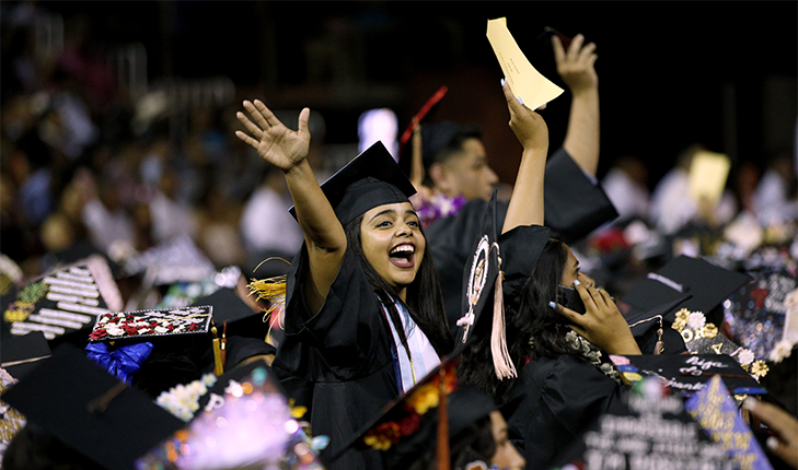 Hispanic student raises her arms triumphantly at commencement ceremony