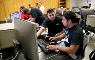 Engineering Students talking and working at a computer in a classroom with other students