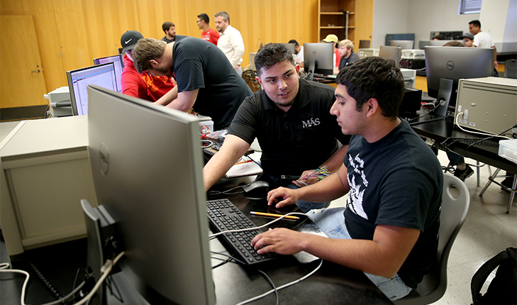 Engineering Students talking and working at a computer in a classroom with other students