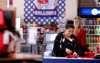 A female Fresno State Bookstore employee standing behind the counter folding shirts.