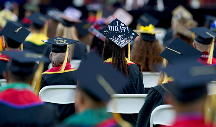 Fresno State graduates sittign with their backs to the camera. A young women's graduation cap is decorated with the words "I did it!"