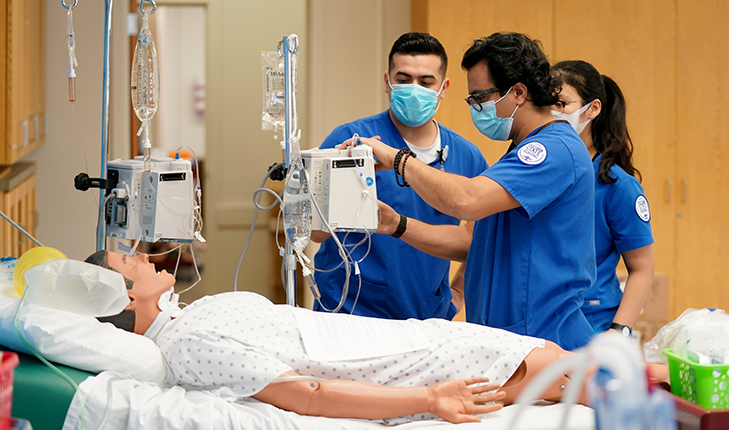 Three student nurses are practicing on a doll.