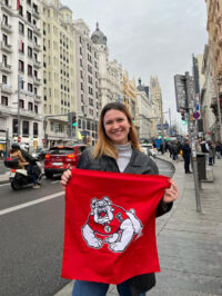 Lillian Hammestrom holds a red flag with the four paw Fresno State Bulldog in studying in Spain.
