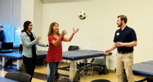 Students helping woman with soccer ball