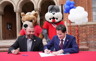 Fresno City College President Robert Pimentel (on the left) and Fresno State President Saul Jimenez-Sandoval sign an agreement to strengthen relations and increase the number of transfer students from the college to the university. School mascots Sam the Ram and TimeOut stand behind the presidents.