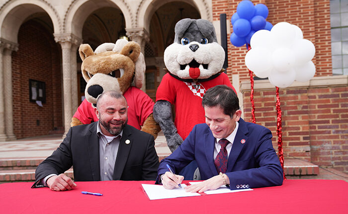 Fresno City College President Robert Pimentel (on the left) and Fresno State President Saul Jimenez-Sandoval sign an agreement to strengthen relations and increase the number of transfer students from the college to the university. School mascots Sam the Ram and TimeOut stand behind the presidents.