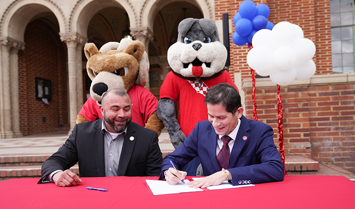 Fresno City College President Robert Pimentel (on the left) and Fresno State President Saul Jimenez-Sandoval sign an agreement to strengthen relations and increase the number of transfer students from the college to the university. School mascots Sam the Ram and TimeOut stand behind the presidents.