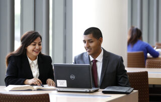 Two students sitting at a table looking at a laptop