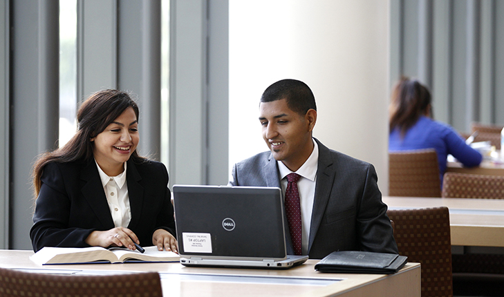 Two students sitting at a table looking at a laptop